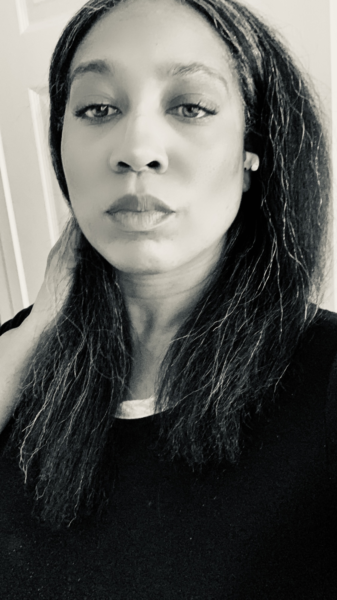 Black and white portrait of a woman with straight, shoulder-length hair, wearing a dark top, looking directly at the camera with a neutral expression.